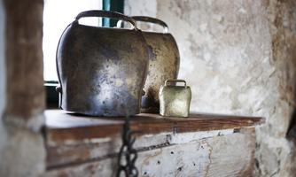 Two old metal weights are placed on a wooden shelf. The texture of the wall and the light create a rustic atmosphere.