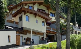 A modern house in Alpine style with wooden decorations and balconies. Surrounded by green trees and a tranquil landscape.