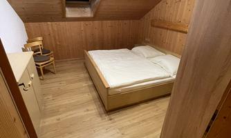 A cozy bedroom with wooden interior. It includes a double bed, a chair, and a dresser.