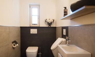 A modern bathroom with a toilet and a sink. There is a small window opening and decorative wall design.