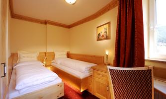 A cozy room with two single beds, a table, and a chair. The walls are light and the curtains are red.