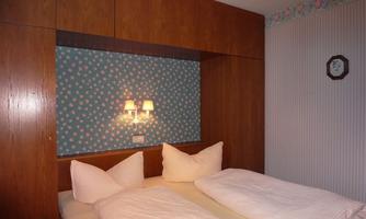 A cozy bedroom with a double bed and decorative pillows. The walls are decorated with blue wallpaper and floral patterns.