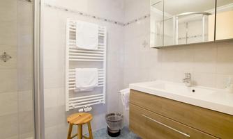 A modern bathroom with a sink, a mirror, and a towel holder. There is a small stool and a laundry basket in the corner.
