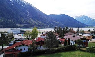 A picturesque landscape with colorful houses at the foot of mountains. In the background, a calm lake flows, surrounded by green meadows and trees.