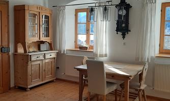 A cozy dining area with a wooden table and chairs. The windows let in a lot of light and the room has a rustic charm.