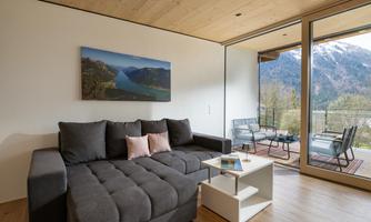 A modern living room with a comfortable sofa and a small table. Large windows offer a splendid view of the mountains and nature outside.