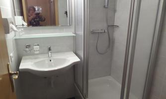 A modern bathroom with a shower, a sink, and large mirrors. The walls are light-tiled, and the design appears clean and functional.