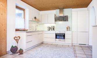 A modern kitchen with white furniture and wooden ceilings. The room is bright and friendly with a carpet on the floor.
