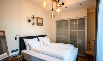 A modern bedroom with a comfortable double bed and stylish lanterns. The walls are light, and there are small decorative elements as well as a wardrobe with glass doors.