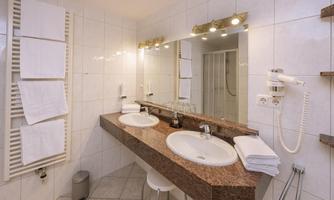 A modern bathroom with a double sink and large mirrors. Fresh towels and a shower are also visible.