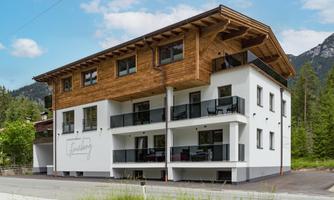 A modern house with wooden cladding and balconies. It is located in a beautiful, nature-friendly environment.