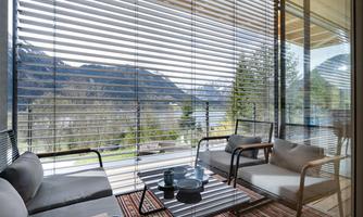 A cozy balcony with modern furniture and a view of the mountains. The large windows let in plenty of light and provide a relaxing atmosphere.