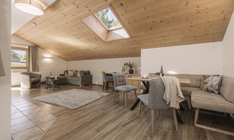 A cozy living area with a wooden ceiling and large windows. There is a dining area as well as a lounge area with modern furniture.
