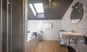 A modern bathroom with a bathtub and a shower. Large windows provide plenty of light and a pleasant atmosphere.