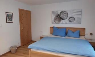 A cozy bedroom with a wooden bed and blue cushions. A modern painting featuring planet motifs hangs on the wall.