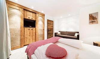 A modern bedroom with a large bed and heart-shaped pillows. The walls are light, and there are wooden details that create a cozy atmosphere.