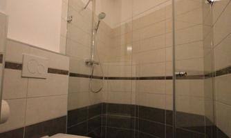 A modern bathroom with a walk-in shower and a toilet. The walls are brightly tiled, and the ceiling has exposed wooden beams.