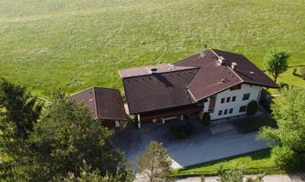 A large house in the rural area, surrounded by green meadows and trees. The sky is clear and the surroundings are peaceful.