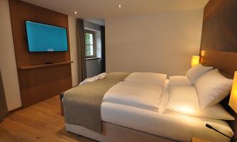 A modern bedroom with two beds, a cozy blanket, and a large wall lamp. A flat-screen television hangs on the wall, providing entertainment in the room.