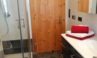 A modern bathroom with a shower and a bathtub. Red towels are placed on the sink and the floor is tiled with dark tiles.