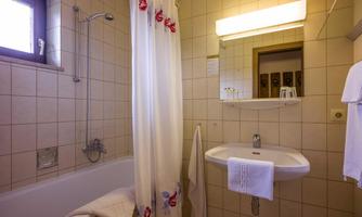 A small bathroom with a bathtub and a shower cabin. There is a mirror and towels are neatly hung up.