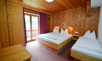A cozy room with wooden walls and two beds. Large windows provide daylight and access to a balcony.