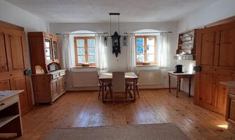 A cozy dining area with wooden cabinets and a large table. Bright windows provide plenty of daylight in a rustic room.