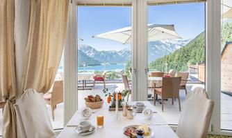 A cozy breakfast table with a view of the mountains and a lake. The terrace is equipped with sun umbrellas and comfortable chairs.