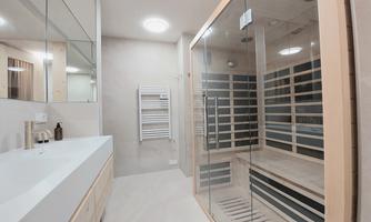 A modern bathroom with a glass shower cabin and a sauna. Bright walls and a large mirror surface give the room a friendly atmosphere.