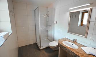 A modern bathroom with a shower and a sink. The walls are brightly tiled and there is a large mirror.