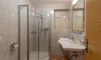 A modern bathroom with a shower cabin and a sink. The walls are tiled in light colors and the fixtures are clean and functional.