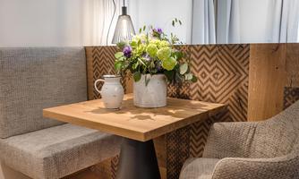 A cozy table with a flower arrangement is in a bright corner. The bench and the chair provide an inviting atmosphere.