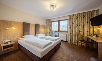 A cozy hotel room with two single beds and wooden paneling. 

A window with a view of the mountains and a desk complete the atmosphere.