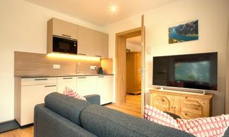 Cozy living room with modern kitchen and television. The decor is bright and friendly, ideal for a relaxed atmosphere.