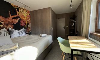 A modern bedroom with a large bed and colorful wall decoration. There is a small desk and a game room with chairs.