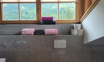 A modern bathroom with a view of nature. Colored towels and toilet paper rolls are lying on the windowsill.