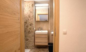 A modern bathroom with wooden details and an elegant sink. The walls are decorated with light stones and there is a large mirror.