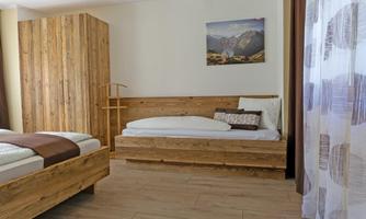 A bright room with wooden furniture and two beds. A picture of mountains hangs on the wall.
