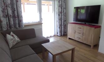 A modern living room with a cozy couch and a wooden table. A large television and floral curtains give the room an inviting atmosphere.