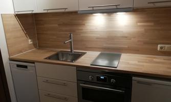 A modern kitchen with light wood surfaces and a stainless steel sink. It has a stove and a dishwasher.