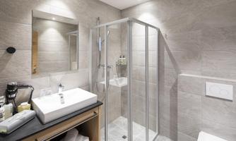 A modern bathroom with a glass shower cubicle and an elegant sink. The walls are adorned with gray tiles, and there is well-placed lighting.