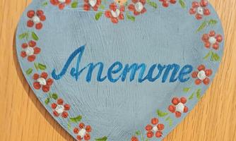 A heart-shaped sign with the inscription "Anemone" in blue letters. It is decorated with small floral motifs.