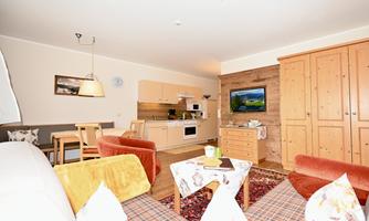A cozy living room with a kitchenette and a dining table. The decor is modern and inviting, with a television and warm colors.