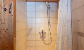 A bright shower with tiles and a shower curtain. The ceiling is made of wood and the shower area looks inviting.