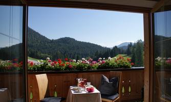 A beautiful view from the balcony of green mountains and blooming flowers. On the table are drinks and snacks, perfect for a relaxing moment.