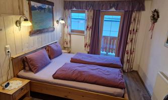 A cozy room with a double bed and purple bed linen. The walls are made of wood, and there is a window with a view outside.