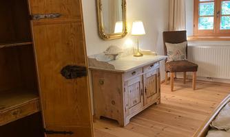 A cozy bedroom with wooden floors and traditional furniture. A mirror and a lamp create a warm ambiance.
