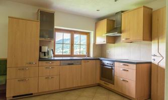 A modern kitchen with wooden cabinets and a large window. The room is bright and welcoming, with a stove and sink.