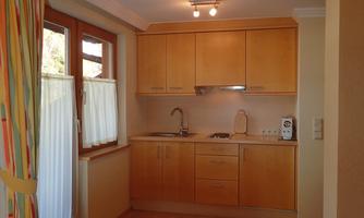 A modern kitchen setup with light wood cabinets and a small window. The space is welcoming and well-lit.