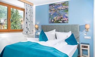 A stylish bedroom with a blue wall and a cozy bed. Decorative cushions and a piece of art featuring water lilies complete the picture.